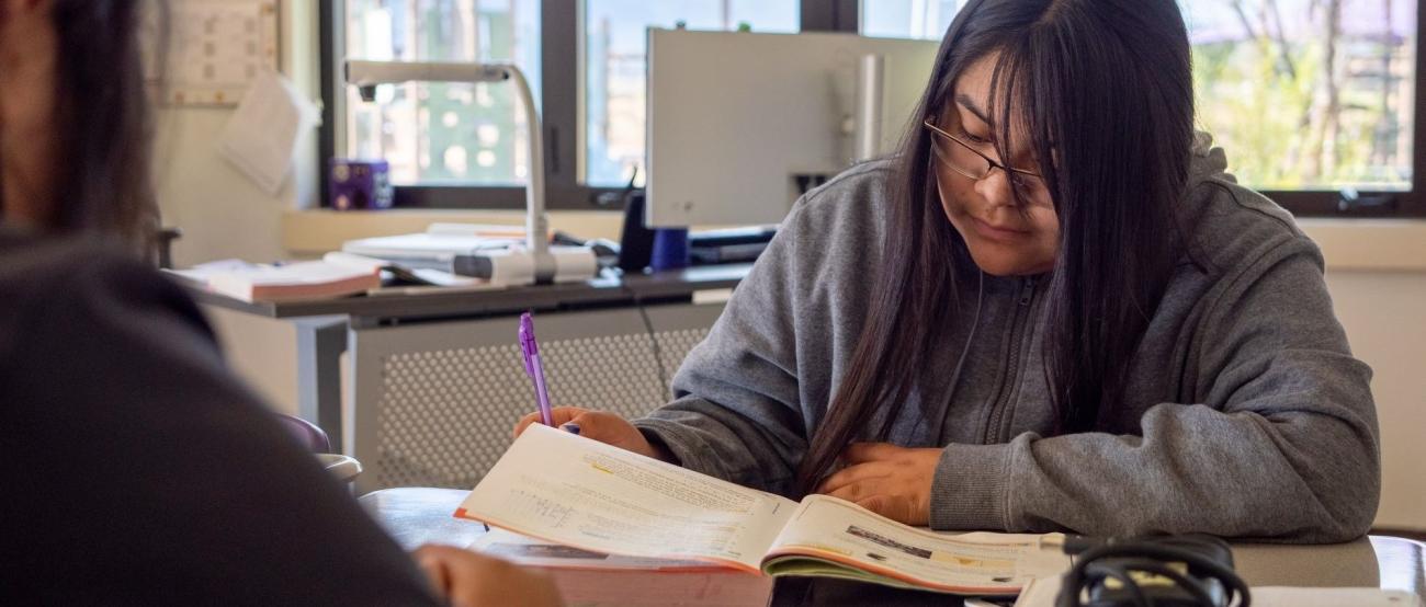Student studying at a desk in class surrounded by books and supplies.