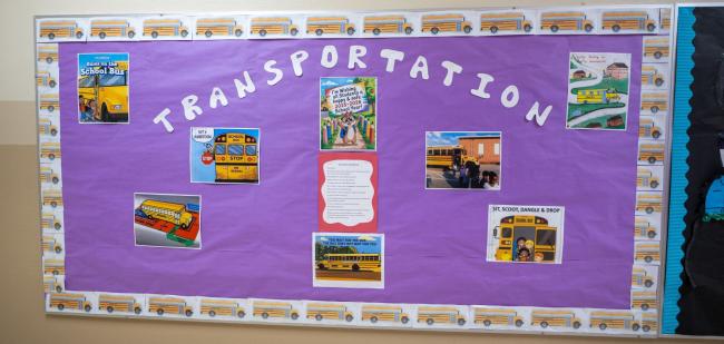 A bulletin board at the school with pictures of school buses and transportation information.
